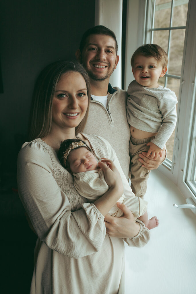 Parents holding their newborn daughter with a toddler boy standing on a window sill in Morristown NJ