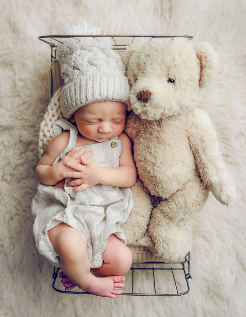 Newborn boy in a hat in a tiny bed with teddy bear